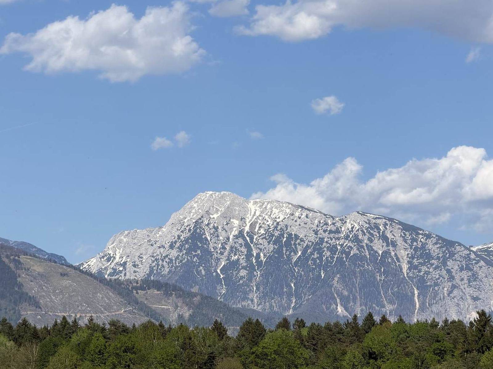 A mountain massif above dark forest under a blue sky