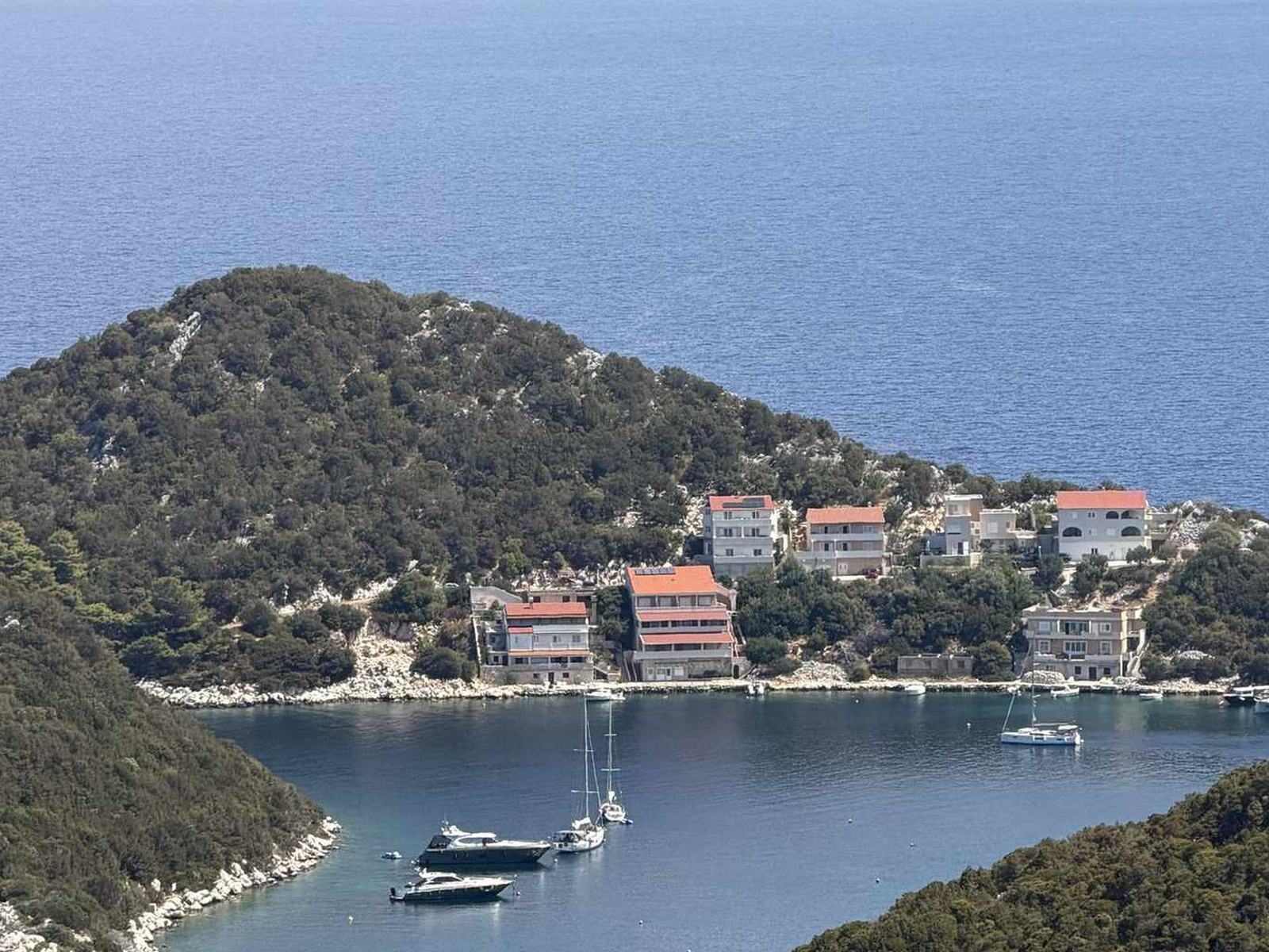 A bay with sailing boats below a wooded slope