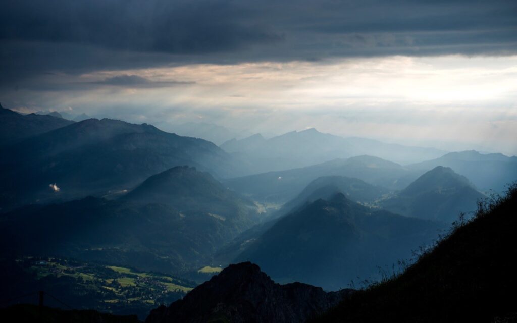 Sončni žarki skozi temne oblake nad hribi
